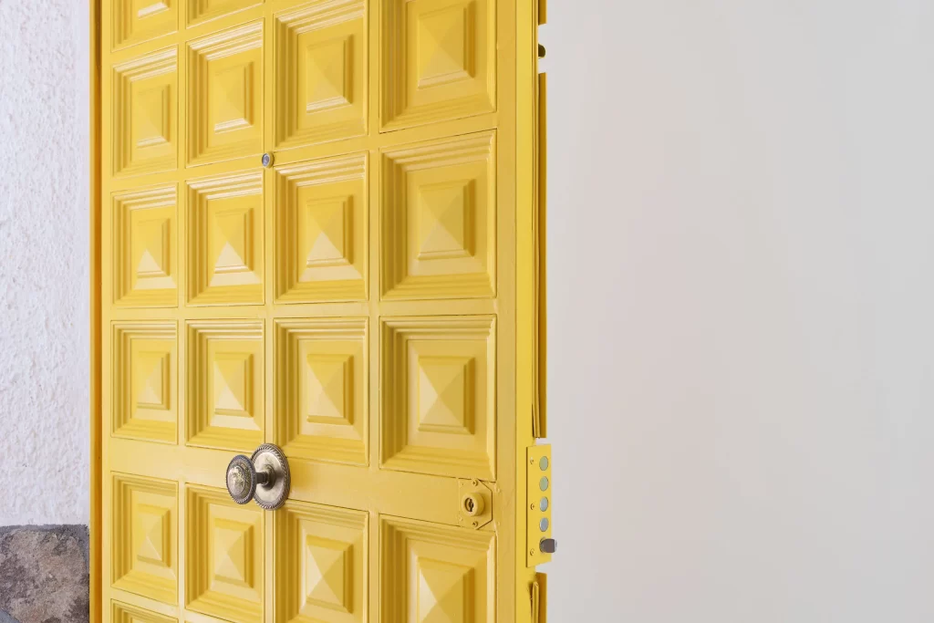 Entrada de la casa con la puerta metálica antigua con relieve, modernizada con color amarillo y tirador envejecido